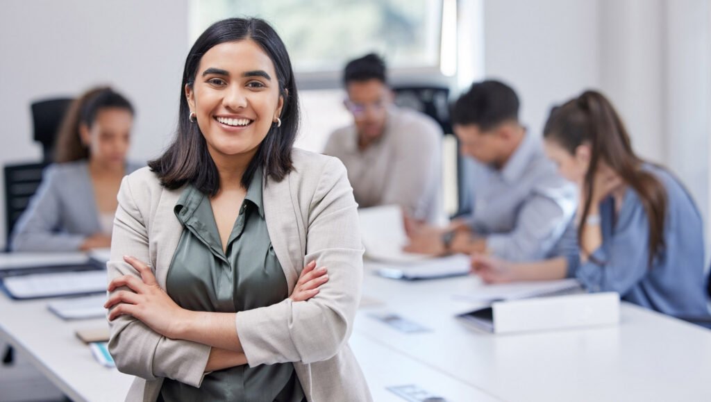 A person standing smiling in front of a desk where other people are working together